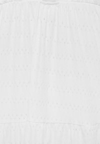 Bílá látka s měkkým, texturovaným povrchem, se svislými, rovnoměrně rozloženými perforacemi. Materiál má na horním okraji nařasenou elastickou část.