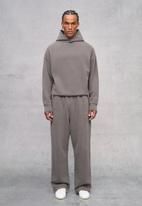 Felpa grigia oversize con collo alto e pantaloni larghi abbinati. Il tessuto sembra morbido con un branding discreto sui pantaloni. Sneakers bianche completano il look.