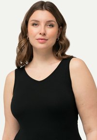 Schwarzes ärmelloses Top mit V-Ausschnitt-Design, aus glattem Stoff gefertigt. Die Passform liegt eng am Körper an und bietet ein schlichtes, klassisches Erscheinungsbild.