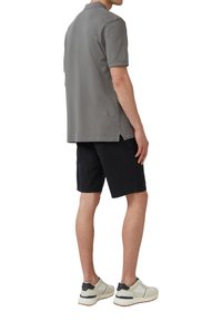 Grijze polo met korte mouwen, gecombineerd met zwarte shorts. Model draagt witte sneakers met marineblauwe accenten. Soepele stoftextuur.