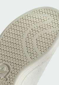 Hvid gummisål til sneakers med et cirkulært stenmønster, teksturerede kanter og et præget logo på hælen.
