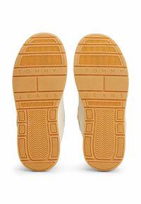 Semelles de chaussures en caoutchouc beige avec un motif texturé. Présente le texte en relief "TOMMY JEANS" et des sections de rainures et de nervures variées.