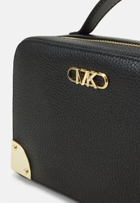 Černá kabelka z korálkované kůže s horním úchytem, zlatým logem a akcenty na rozích. Obdélníkový tvar, uzavírání na zip nahoře.