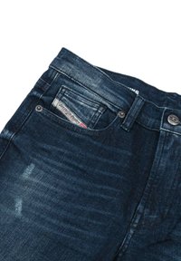 Temno modri jeans klasičnega kroja, ki imajo zbledelo teksturo, oznako na zadnji žep in kovinske gumbe na pasu.