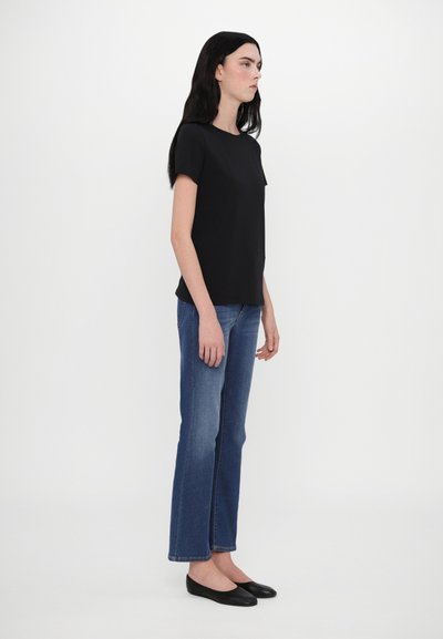 Sort kortærmet t-shirt med rund hals, parret med mellemblå lige bukser og sorte flade sko. Glat stof og enkelt design.
