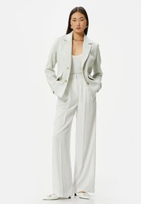 Vit skräddarsydd blazer i ett strukturerat tyg, matchad med en vit ribbad tanktop och vida byxor. Accessoarerna inkluderar guldfärgad hårdvara.