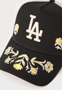 Svart basker med vitt "LA"-logotyp, prydd med gula blommönsterbroderier på framsidan och sidorna. Tillverkad av tyg med en strukturerad form.