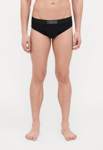 Black men’s briefs made of soft material, featuring a textured elastic waistband with the Versace logo displayed prominently.