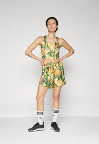Athletic two-piece outfit featuring a crop top and shorts with a yellow floral pattern, made of lightweight fabric, complemented by black sneakers.