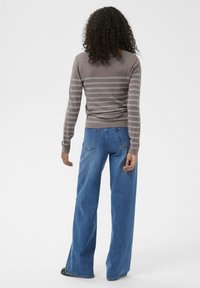 Maglione grigio a righe con maniche lunghe, abbinato a jeans in denim blu a vestibilità ampia. La trama sembra morbida, con una vestibilità rilassata.