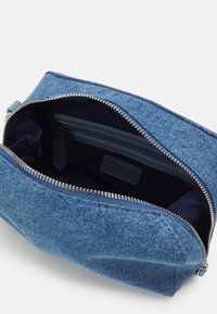 Denimpåse med dragkedja, som har ett mörkt inre och en liten ficka inuti. Hela väskan är i blått med en strukturerad yta.