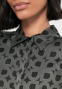 Čierna blúzka s monochromatickým geometrickým vzorom rôznych zaoblených tvarov, klasickým golierom a zapínaním na gombíky. Hladká textúra.