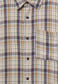Koszula w kratę w kolorach beżowym, brązowym, granatowym i jasnoniebieskim. Z kołnierzykiem, zapięciem na guziki oraz kieszenią na piersi. Teksturowany materiał z wzorem w kratę.