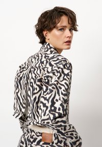 Zwarte en crèmekleurige abstracte denimjas met een tailored fit, voorzien van een leren label op de achterkant en zichtbare stikseldetails.