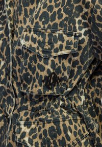 Giacca in denim con stampa leopardata nei toni del tortora e del nero. Presenta una tasca sul petto, un logo stilizzato e un tessuto testurizzato con dettagli di cucitura visibili.