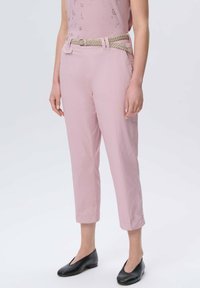 Jasnoróżowe, krótkie spodnie z plecionym beżowym paskiem, z dwoma przednimi kieszeniami i gładką fakturą, w połączeniu z czarnymi płaskimi butami.