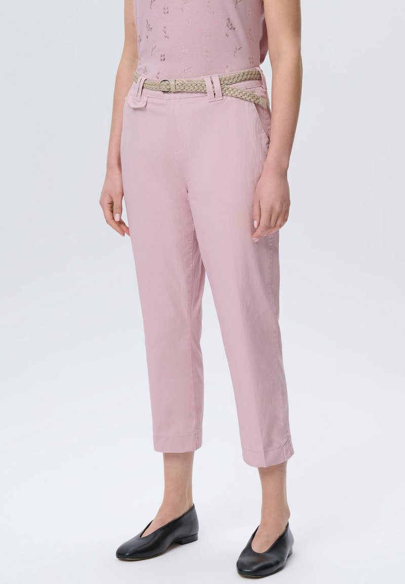 Jasnoróżowe, krótkie spodnie z plecionym beżowym paskiem, z dwoma przednimi kieszeniami i gładką fakturą, w połączeniu z czarnymi płaskimi butami.