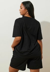 Svart oversized t-shirt i bomull, kombinerad med matchande svarta shorts. Har korta ärmar och en avslappnad passform, visad bakifrån.