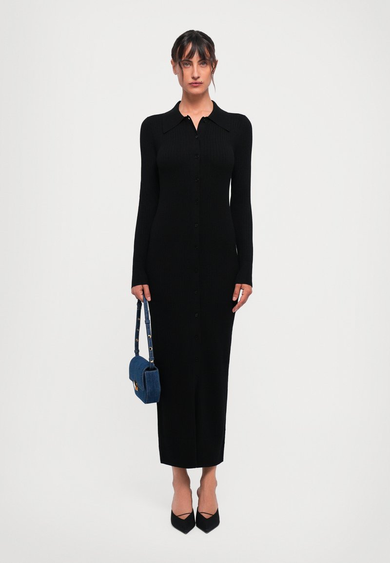 Vestido negro de manga larga con canalé, cuello de camisa y botones en la parte frontal. Combinado con un bolso de mezclilla azul y tacones negros de punta.