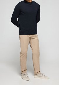 Laivastonsininen pyöreäkauluksinen neulepaita pitkine hihoineen, beige kapealahkeiset housut sekä vaaleat lenkkarit, joissa neulepaidassa hienovarainen logodetaili.