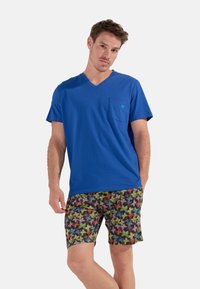 Blå bomulds V-hals t-shirt med en brystlomme, parret med sorte shorts med et farverigt sommerfugl mønster. Blød tekstur og afslappet pasform.