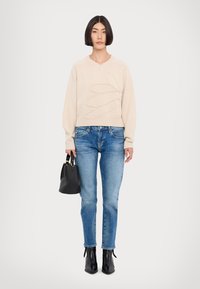 Pull en tricot beige avec un motif texturé, associé à un jean bleu clair. Un sac à main noir et des bottines à bout pointu complètent le look.