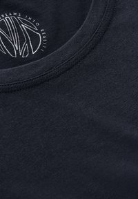 T-shirt di cotone nero con collo rotondo, caratterizzato da testo stampato bianco in un design circolare all'interno del colletto. Texture liscia.