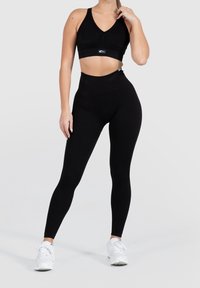 Black sports bra and high-waisted leggings made from ribbed fabric, featuring a snug fit and soft texture. Worn with white athletic shoes.