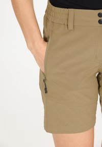 Khaki shorts dengan pinggang elastis, dua kantong samping, dan kantong ritsleting. Memiliki tekstur halus dan detail jahitan yang rapi.