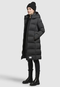 Giacca a vento nera con cappuccio, dotata di chiusura con zip e design trapuntato. Accompagnata da un berretto a maglia nero e stivaletti alla caviglia.