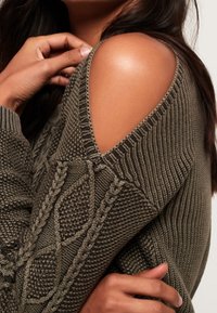 Olivově zelený pletený svetr s designem s odkrytými rameny, se strukturálními vzory a kabelkovým pletením na rukávech.