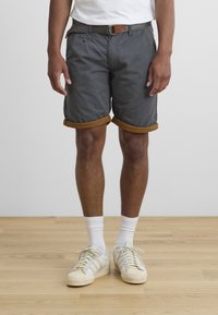 Gray fabric shorts with rolled hem details in brown, featuring a belt with a metallic buckle, worn over white socks and sneakers.