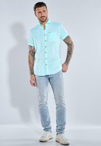 Helles blaues Kurzarmhemd mit Brusttasche, mit Knopfleiste, kombiniert mit hellblauen Jeans und weißen Turnschuhen.