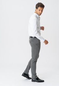 Grå skræddersyede bukser lavet af et struktureret stof, med et slim fit, sidelommer og et sort bælte. Sammen med en hvid skjorte med knapper og sorte sko.