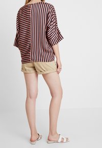 Haut ample à rayures verticales rose foncé et marine, associé à un short beige. Caractérisé par des manches larges et un dos simple.