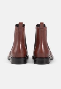 Bottes Chelsea en cuir marron avec panneaux élastiques latéraux, bout rond et semelle en caoutchouc noir. Tirant à l'arrière pour faciliter l'enfilage. Fini lisse.