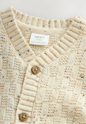 Off-white knitted sweater with a textured pattern, featuring a V-neck, ribbed collar, and round, embossed gold button on the front.