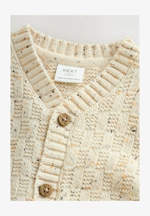 Kremasti pleteni džemper s teksturiranim uzorkom, koji ima V-izrez, rebrasti ovratnik i okrugli, utisnuti zlatni gumb sprijeda.
