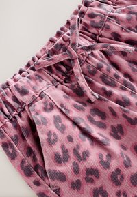 Ružové krátke nohavice z manšestru s čiernym leopardím vzorom, vybavené elastickým pásom a sťahovacou šnúrkou. Viditeľné výrazné textúrne a vzorové detaily.