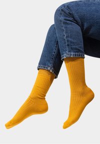 Żółte skarpetki ribbed wykonane z miękkiego materiału, o długości do połowy łydki i elastycznym mankietem. Noszone z niebieskimi dżinsami.