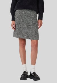 Schwarz-weiße gepunktete knielange Röcke, getragen mit weißen Socken und schwarzen klobigen Loafers, kombiniert mit einem schwarzen, flauschigen Pullover.