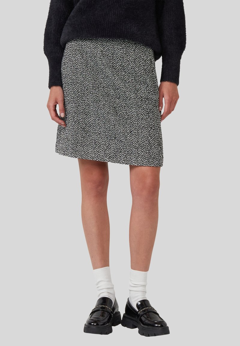 Schwarz-weiße gepunktete knielange Röcke, getragen mit weißen Socken und schwarzen klobigen Loafers, kombiniert mit einem schwarzen, flauschigen Pullover.