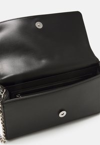 Borsa a tracolla rettangolare nera realizzata in pelle liscia. Presenta una chiusura a scatto argentata e una tracolla a catena, con un compartimento con zip all'interno.