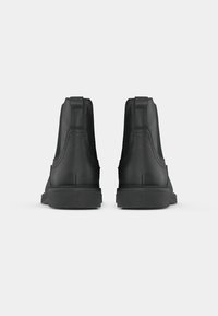 Bocanci negri până la glezne, cu un finisaj texturat, panouri laterale elastice și tălpi plate din cauciuc, având un design minimalistic și o formă structurată.