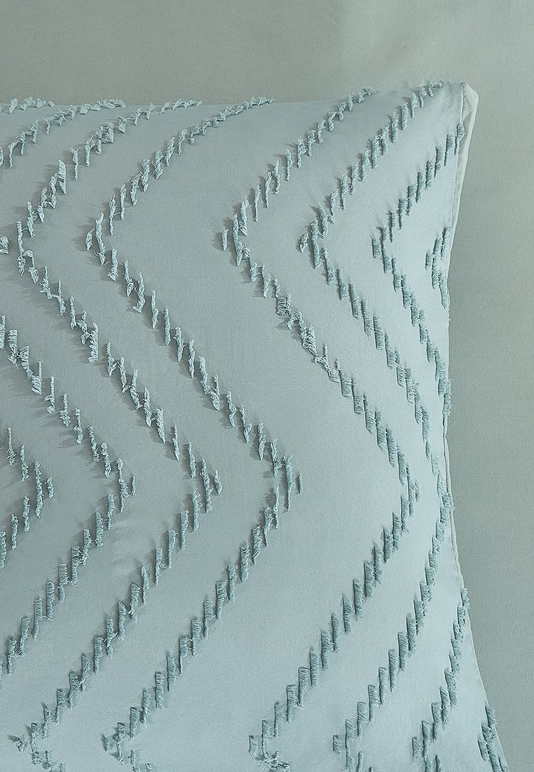 Coussin carré en tissu bleu clair, arborant un motif en zigzag avec des franges texturées le long du design, surface douce.