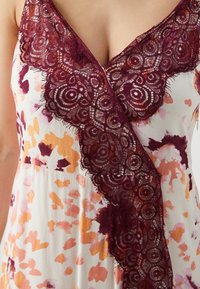 Blumenkleid mit weißem Hintergrund, das orangefarbene und rosa Flecken aufweist, sowie einen tief burgundenen Spitzenbesatz entlang des Ausschnitts.