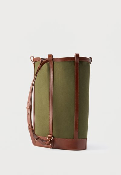 Πράσινη τσάντα tote από καμβά με καφέ δερμάτινα λουριά, βάση και περιθώρια, όρθια σε λευκό φόντο.