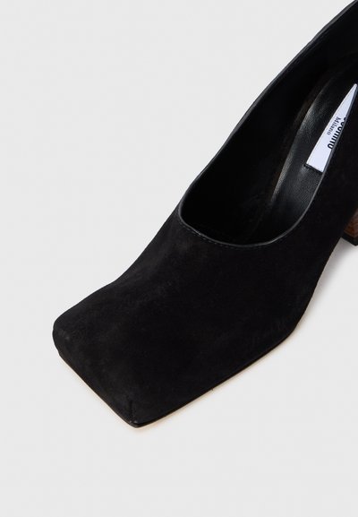 Pantofii negri din suede, cu toc înalt, vârf pătrat, guler rotunjit și toc din lemn bloc. Textura netedă adaugă eleganță designului.