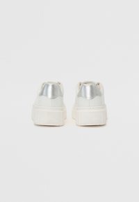 Sneaker bianche con suola testurizzata presentano un accento lucido in argento sul tallone e un materiale superiore liscio, progettate per un abbigliamento casual.