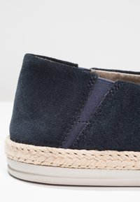 Espadrille en daim bleu marine avec une semelle en jute tressé et un dessous en caoutchouc lisse. Dotée de panneaux latéraux élastiques pour un enfilage facile.